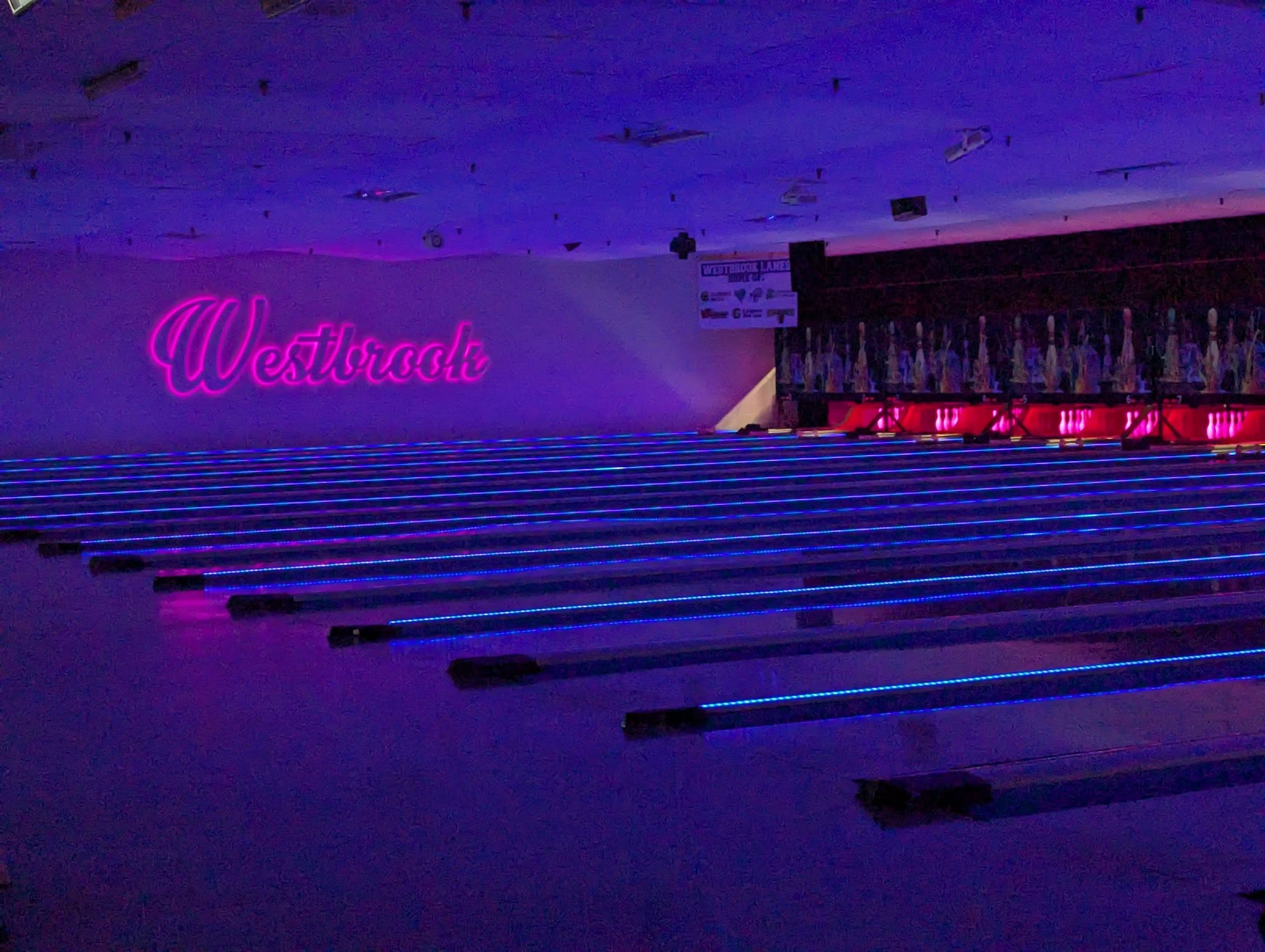 Cosmic bowling at Westbrook Lanes — glowing blue lanes under blacklight with the pink neon Westbrook sign